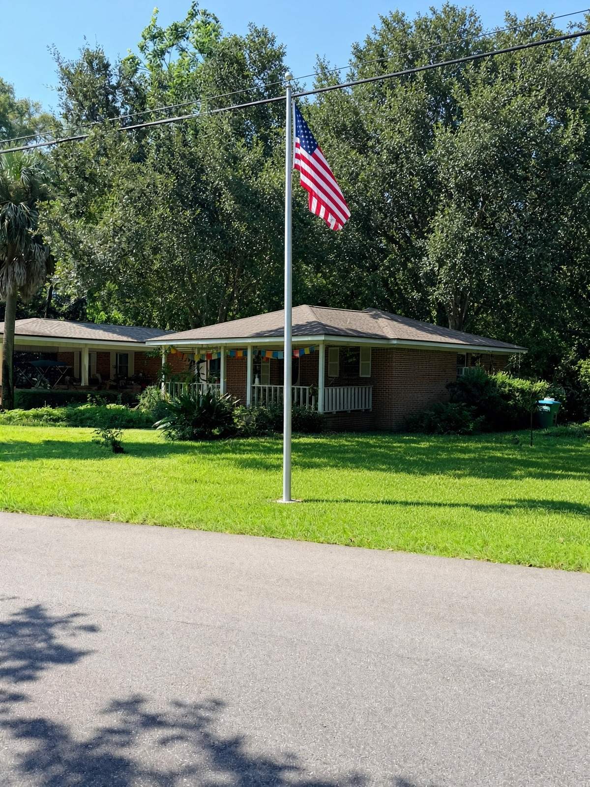 Our single-story brick house after Hurricane Ivan, with an American flag on a tall metal flagpole, a wide green front lawn, and trees behind the house